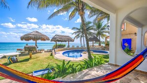 A pool area with a hammock, lounge chairs, and thatched umbrellas overlooking the ocean. - Beautiful pool side ground floor unit with direct beach access , WiFi and AC. (Akumal)