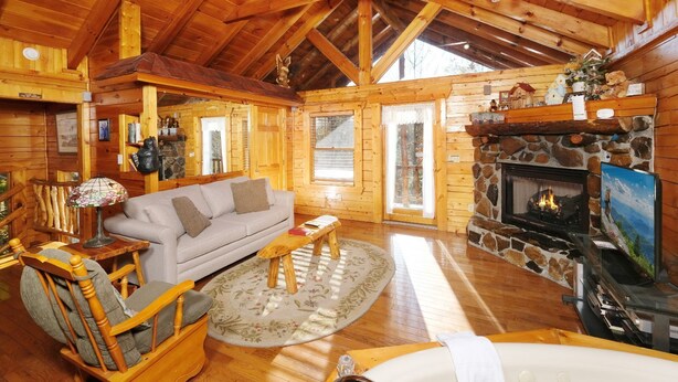 A cozy cabin interior with a stone fireplace, wooden furniture, and a large window. - First Flight - Pool Table & Hot Tub! (Sevierville)