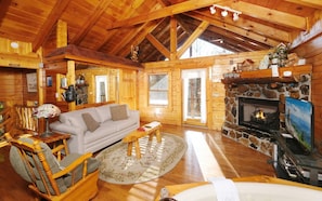 A cozy cabin interior with a stone fireplace, wooden furniture, and a large window.