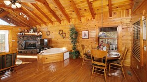 A cozy cabin interior with a stone fireplace, a hot tub, wooden furniture, and a dining area. - First Flight - Pool Table & Hot Tub! (Sevierville)