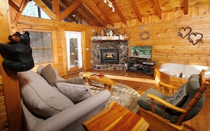 A cozy log cabin interior with a fireplace, a television, and a bathtub.