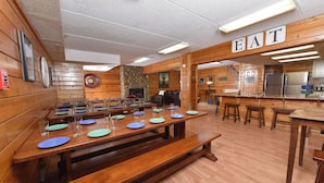 A rustic dining area with wooden tables and benches, a stone fireplace, and a kitchen area with stainless steel appliances.