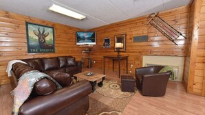 A cozy log cabin interior with a leather sofa, a coffee table, a fireplace, and wooden walls.