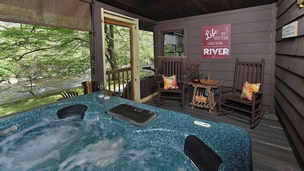 A hot tub area with a view of a river, wooden deck chairs, and a sign that says "Life is better on the river."