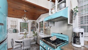 Una cocina con estufa turquesa, gabinetes blancos y un comedor con mesa y sillas.