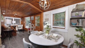 Una habitación acogedora y bien iluminada con techo de madera, una mesa redonda con platos y un jarrón de flores, y una zona de estar con sofá y sillones.