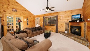 A cozy log cabin interior with a fireplace, a television, and a ceiling fan. - Mountain Blessing - Relax on the Screened Porch (Sevierville)