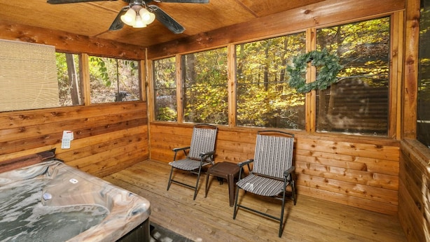 A wooden cabin with a hot tub, two striped chairs, and a view of autumn foliage through large windows. - Mountain Blessing - Relax on the Screened Porch (Sevierville)