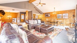 A log cabin interior with a leather sofa, wooden dining table, and a ceiling fan.
