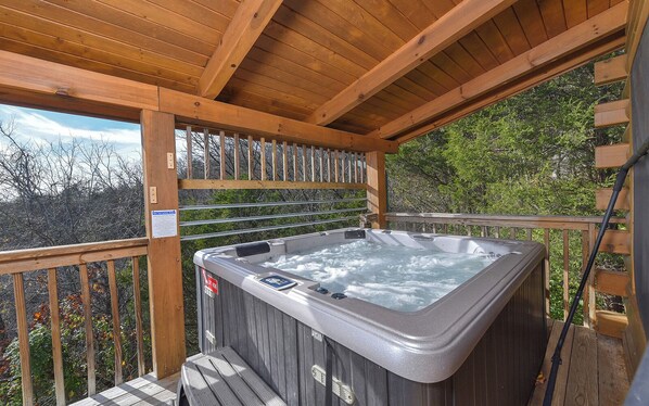 A hot tub on a wooden deck with a view of trees and a cloudy sky.