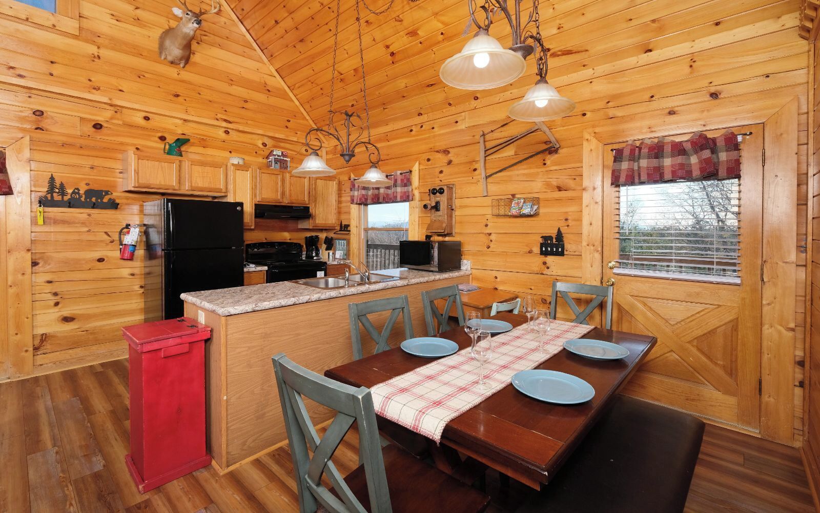 Une cabane en bois comprenant une cuisine, un coin repas et un placard utilitaire rouge.