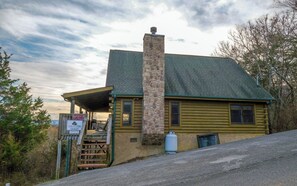 A cabin with a stone chimney, a porch, and a sign indicating it is a cabin with a view. - Pioneer Place - Arcade Games, Mountain Views, Hot Tub (Sevierville)