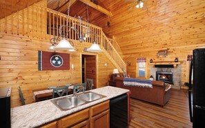 A cozy cabin interior with a kitchen, dining area, and a fireplace.
