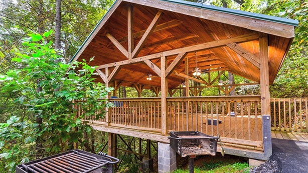 Una cabaña de madera con terraza, una parrilla y una base de piedra.