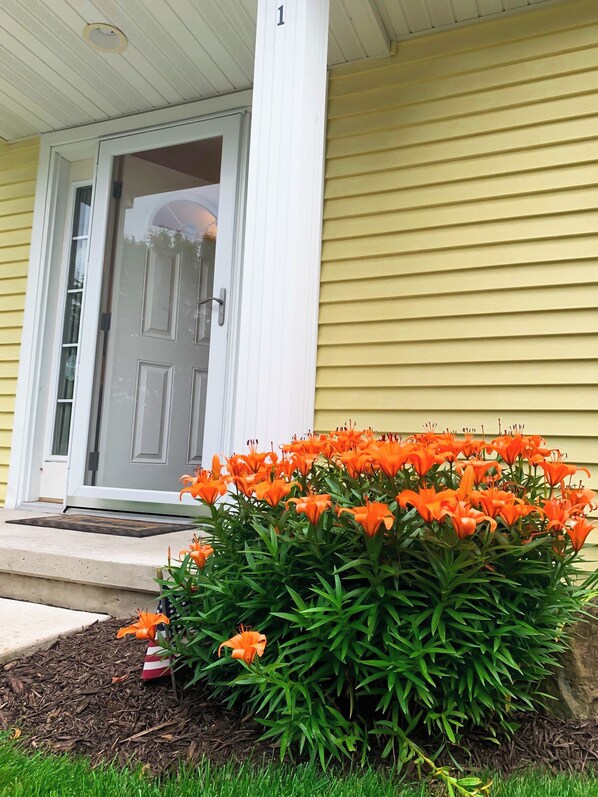 Una casa con puerta principal, el número 1 en la puerta, y un parterre con flores naranjas.