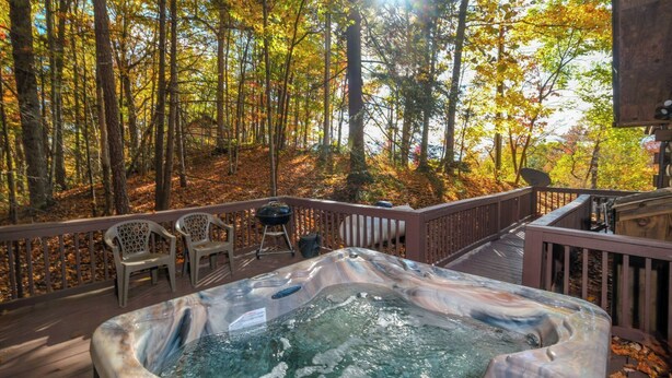 A hot tub on a wooden deck surrounded by trees with autumn foliage.