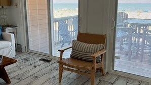 A room with a wicker chair, a patterned rug, and a view of the beach through large glass doors. - Beachfront Baby💛 Beautiful & New!🌟The only way to stay @ the beach❣️Spacious  (Dewey Beach)