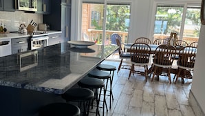 A modern kitchen with dark cabinets, a large island with bar stools, and a dining area with wooden chairs and a table. - Beachfront Baby💛 Beautiful & New!🌟The only way to stay @ the beach❣️Spacious  (Dewey Beach)