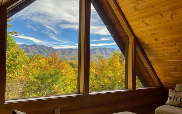 A room with a large window offering a view of autumn foliage and mountains.