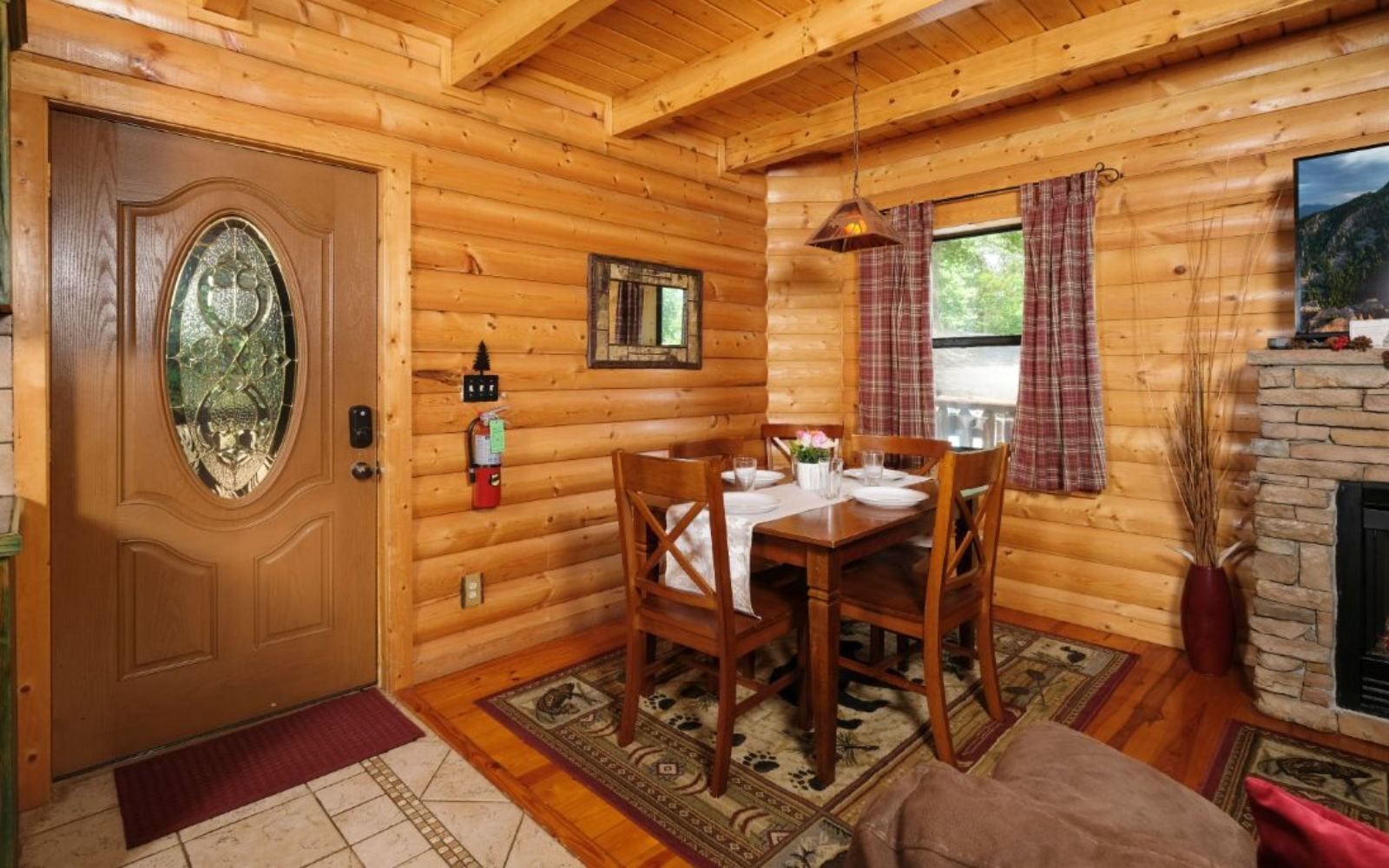 Ein Holzblockhaus-Innenraum mit Essbereich, Kamin und einer Tür mit dekorativem Glasfenster.