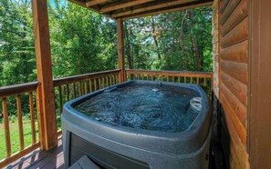 A hot tub on a wooden deck with a wooden railing, surrounded by lush greenery.