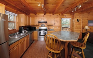 Cozy cabin-style kitchen with a stove, microwave, and sink, offering a warm atmosphere and a view of the surrounding forest.