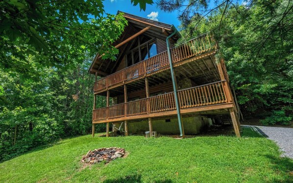 A wooden cabin with a balcony, surrounded by lush greenery.