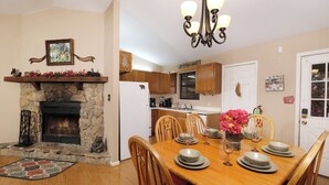 A dining room with a stone fireplace, wooden dining table, chairs, and a chandelier. - Serenity - Pet-Friendly, Xbox, Keurig, Outdoor Hot Tub, Wood-Burning Fireplace (Pigeon Forge)