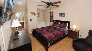 A bedroom with a bed, a nightstand, a chair, a ceiling fan, and a wall-mounted TV. - Serenity - Pet-Friendly, Xbox, Keurig, Outdoor Hot Tub, Wood-Burning Fireplace (Pigeon Forge)