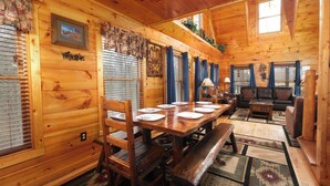 A wooden cabin interior with a dining table set for four, a sofa, and a bench. - The Looney Bin - Hot Tub, Game Loft, Jetted Tub Suite & Wooded Views (Sevierville)