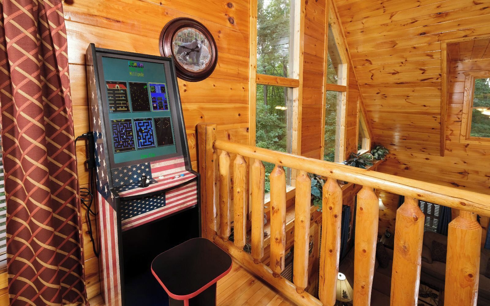 A wooden cabin interior with a gaming console, a clock, and a view of the forest.