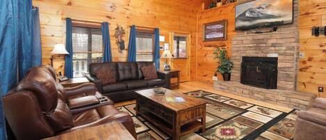En mysig timmerstuga med en öppen spis, en lädersoffa och ett stort träbord.