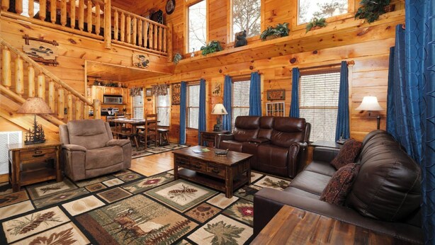 A cozy cabin interior with a wooden staircase, a dining area, a living room with a sofa and chairs, and a kitchen. - The Looney Bin - Hot Tub, Game Loft, Jetted Tub Suite & Wooded Views (Sevierville)