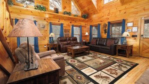 A cozy log cabin interior with a fireplace, leather sofas, and a large rug. - The Looney Bin - Hot Tub, Game Loft, Jetted Tub Suite & Wooded Views (Sevierville)