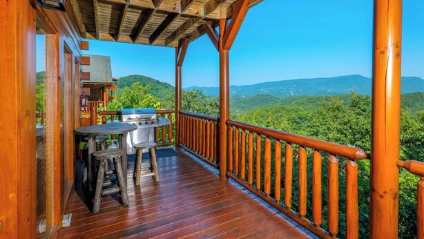 Un patio in legno con un barbecue e un tavolo, con vista su un paesaggio montuoso.