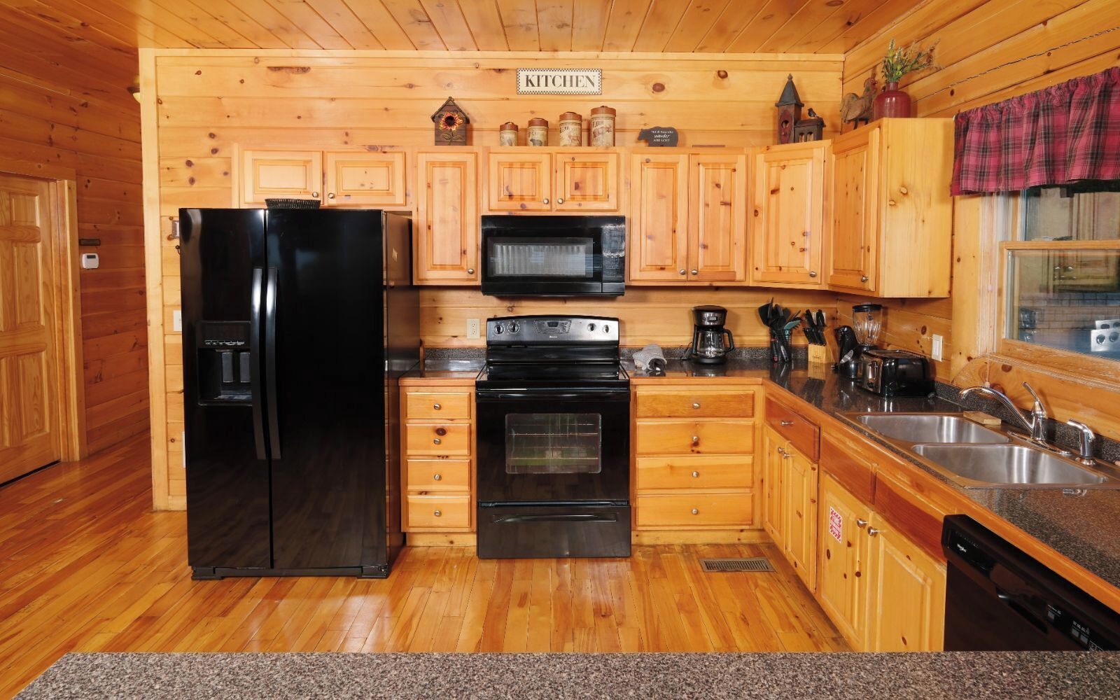 A wooden-paneled kitchen with a black refrigerator, stove, and microwave.