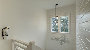 A staircase with white railings and a wall-mounted fire extinguisher. - Moonsong is in a great location, is golf cart accessible and just a short drive (Port Aransas)