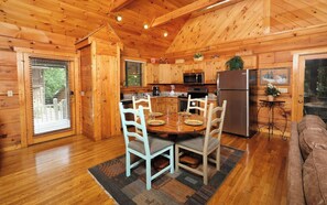 A wooden cabin interior with a dining area, kitchen, and a cozy living space.