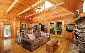 A wooden cabin interior with a living room, kitchen, and a stone fireplace.