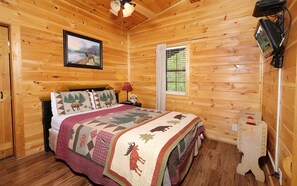 A wooden cabin bedroom with a bed, a nightstand, a lamp, a window with blinds, and a ceiling fan.