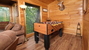 Ett mysigt rum med trägolv, en lädersoffa, ett fotbollsspel, en lampa och ett hjorthuvud som hänger på väggen.