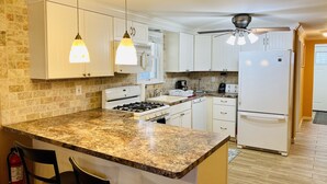 A kitchen with white cabinets, a granite countertop, a gas stove, a microwave, a refrigerator, and a ceiling fan. - Upscale and Cozy Ocean Block Home w/ Free Parking, BBQ, Patio, Outdoor Shower (Seaside heights)