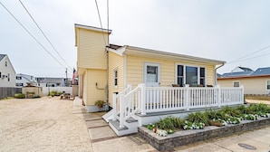 A single-story house with a front porch, a small garden area, and a flag. - Upscale and Cozy Ocean Block Home w/ Free Parking, BBQ, Patio, Outdoor Shower (Seaside heights)