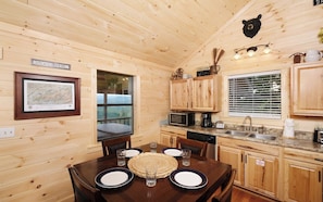 A wooden cabin with a dining table set for four, a kitchen with basic appliances, and a map on the wall.