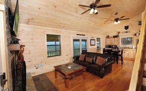 A wooden cabin interior with a living room, dining area, kitchen, and a balcony with a view.