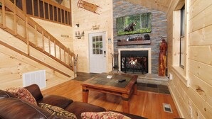 Ein gemütliches Blockhaus-Interieur mit einer Holztreppe, einem Kamin, einem Fernseher und einem Ledersofa.