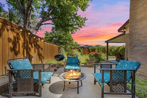 An outdoor patio with a fire pit, seating area, and a wooden fence.