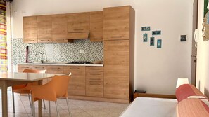 A compact kitchen with wooden cabinets, a tiled backsplash, and a dining area with orange chairs.