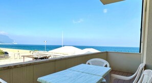 A balcony with a view of the beach, a table, and chairs.