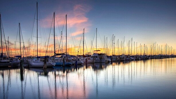 Una marina con diverse barche a vela ormeggiate in acque calme al tramonto.